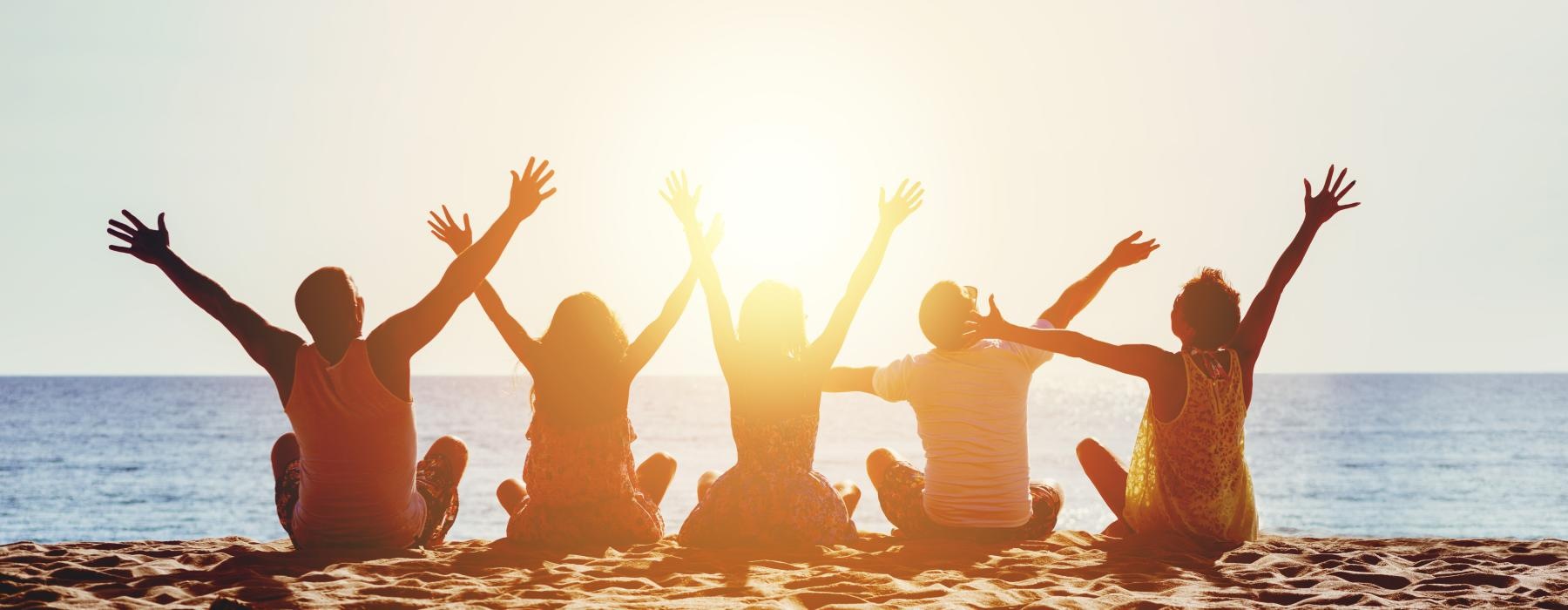 a group of people sitting on a beach with their arms raised
