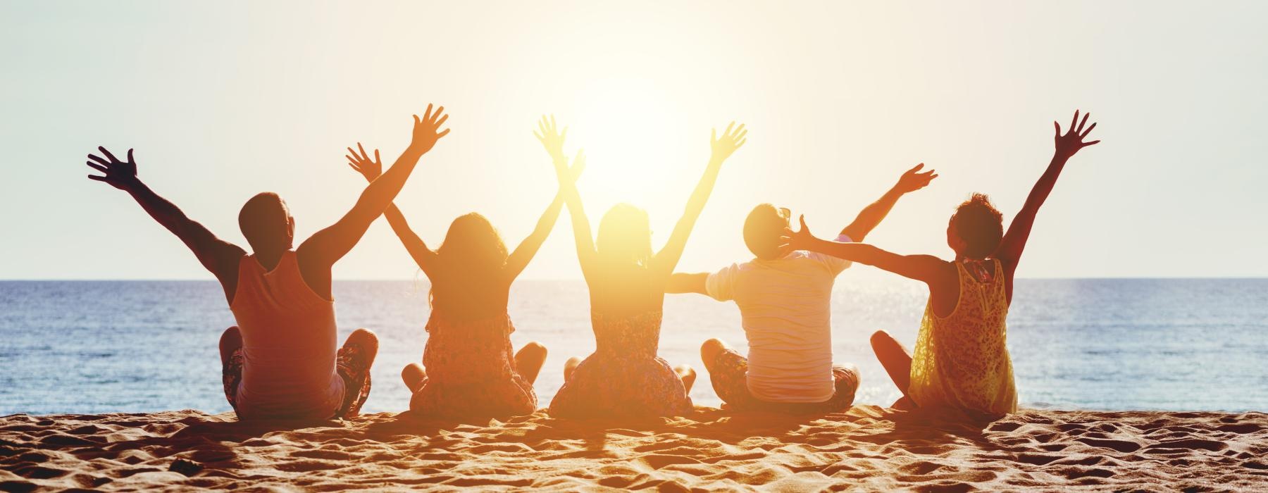 a group of people sitting on a beach with their arms raised